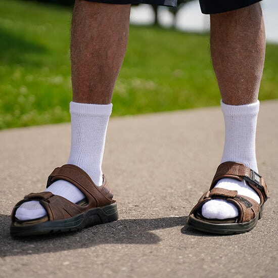 A person wearing white crew socks and brown sandals